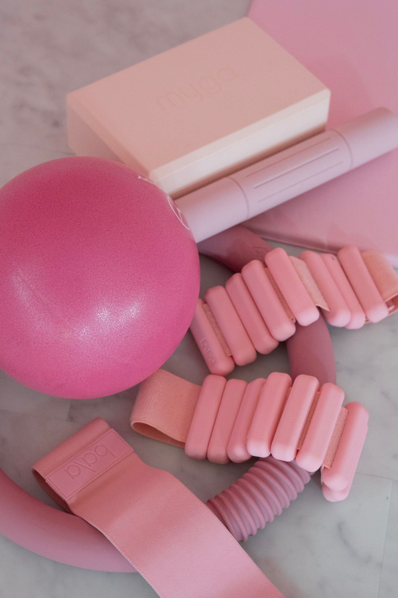 Pink Pilates props including ball, ring, block, bands, and ankle weights