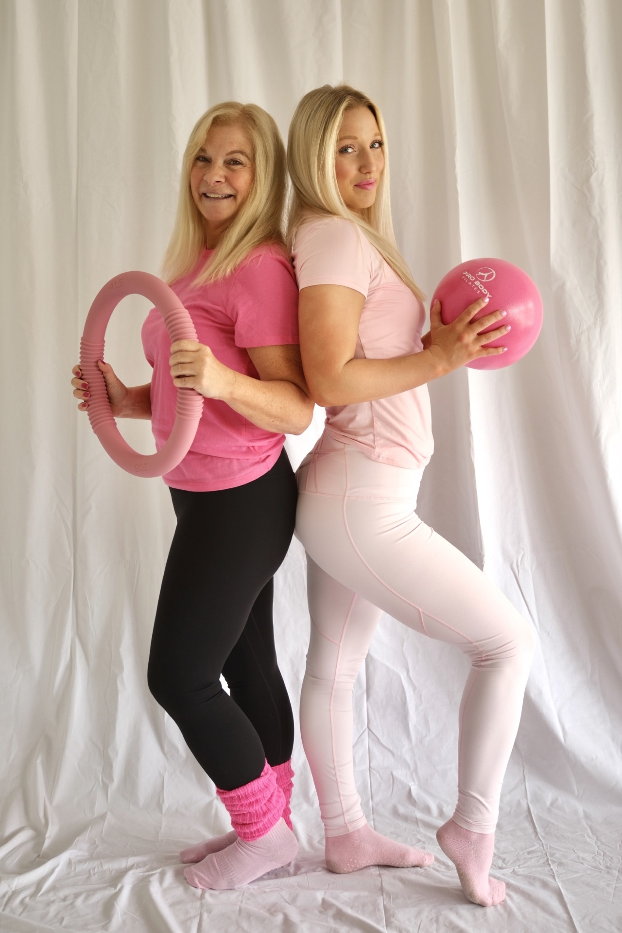 Two Glow and Flow instructors back to back holding a Pilates ring and ball
