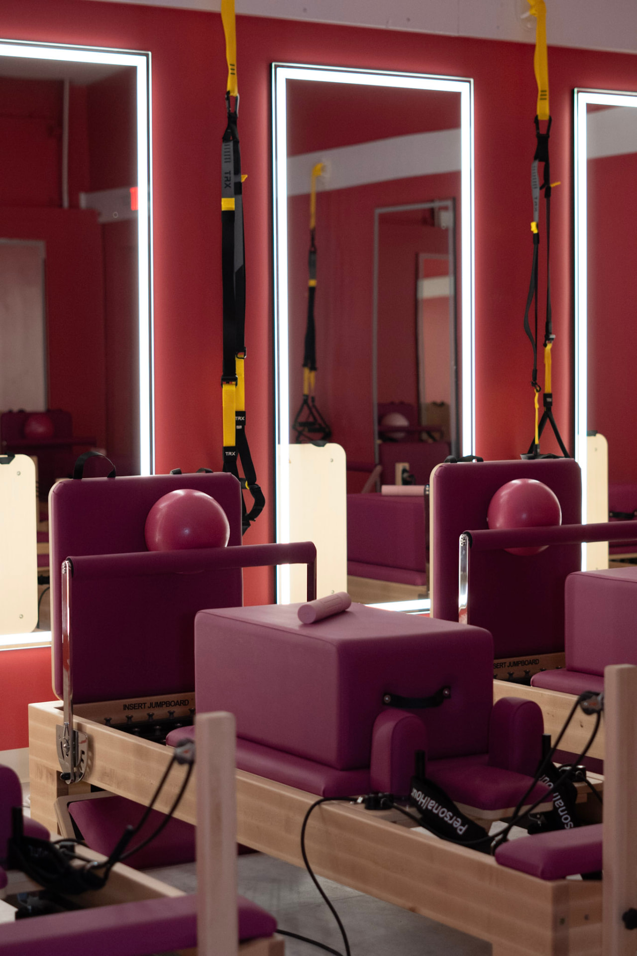 Pink reformers, TRX straps, and lit mirrors in the Glow and Flow reformer room