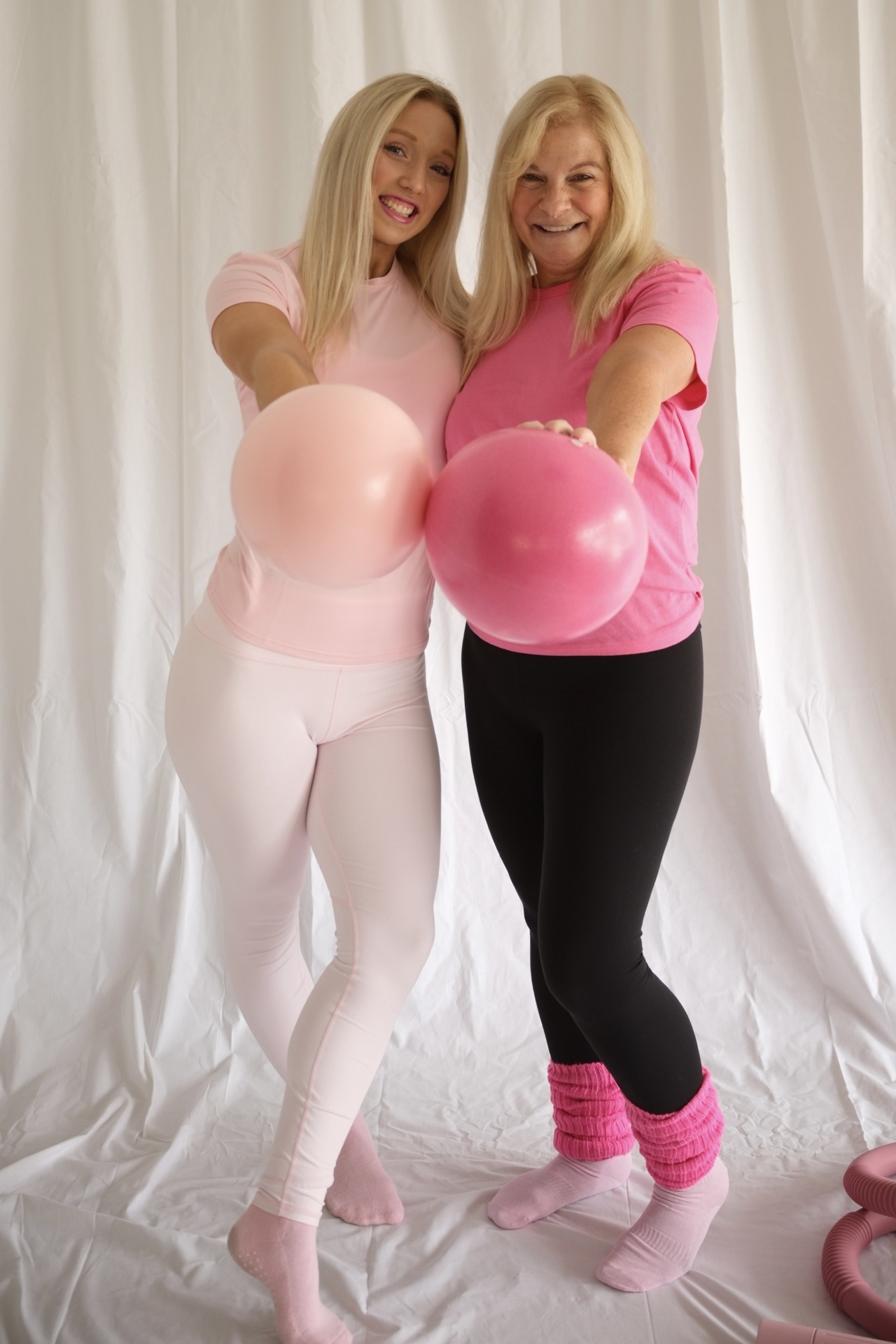 Two Glow and Flow instructors smiling and holding pink Pilates balls