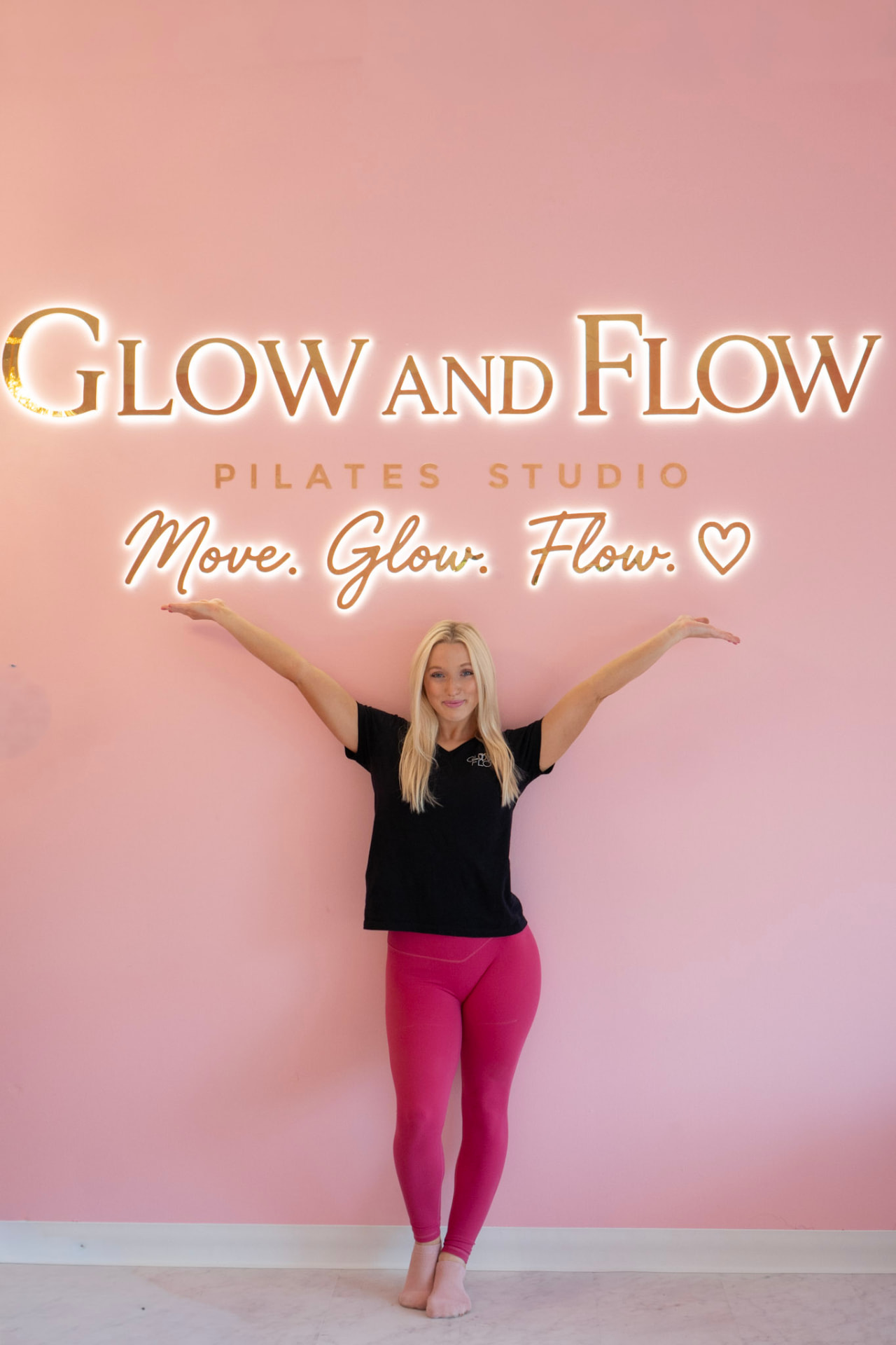 Glow and Flow instructor with arms outstretched in front of the studio's pink Move Glow Flow sign
